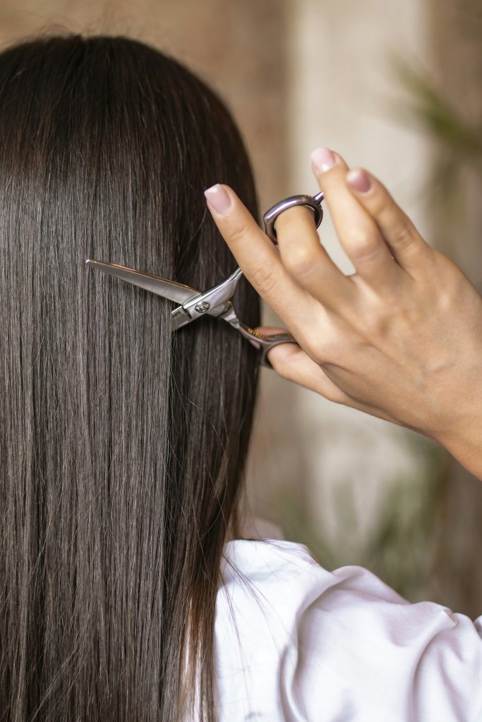 A hand holding open hair-cutting shears against a dark salon backdrop.